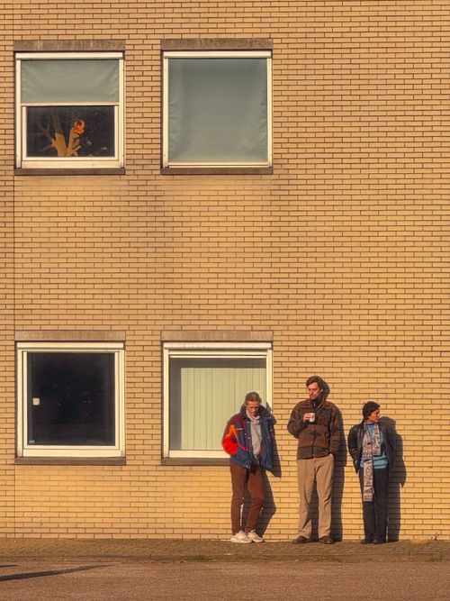Free Three people enjoying an afternoon chat by a sunlit brick wall. Stock Photo