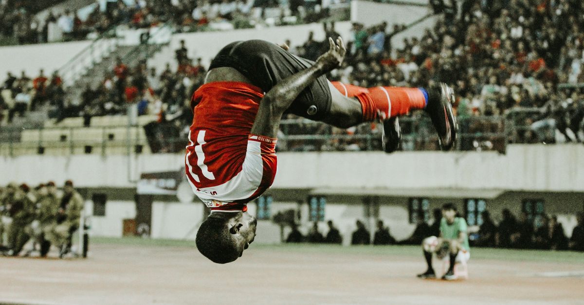 A soccer player performs a dynamic flip during a match, showcasing athletic skill and excitement.