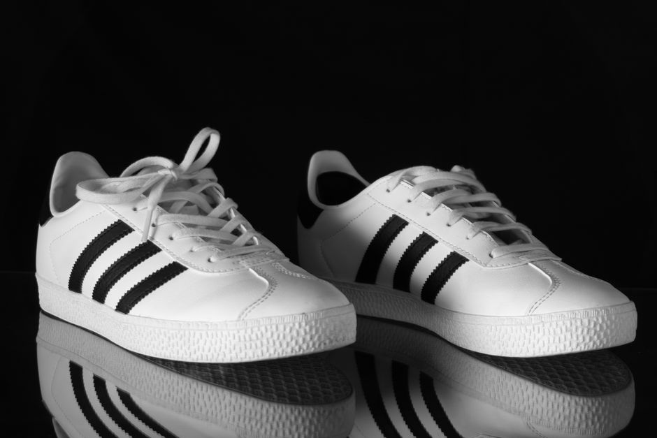 Classic white sneakers with black stripes reflecting against a dark background.