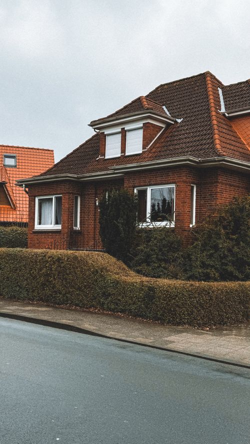 Free A cozy red brick house with a sloped roof and trimmed hedges in a suburban neighborhood. Stock Photo