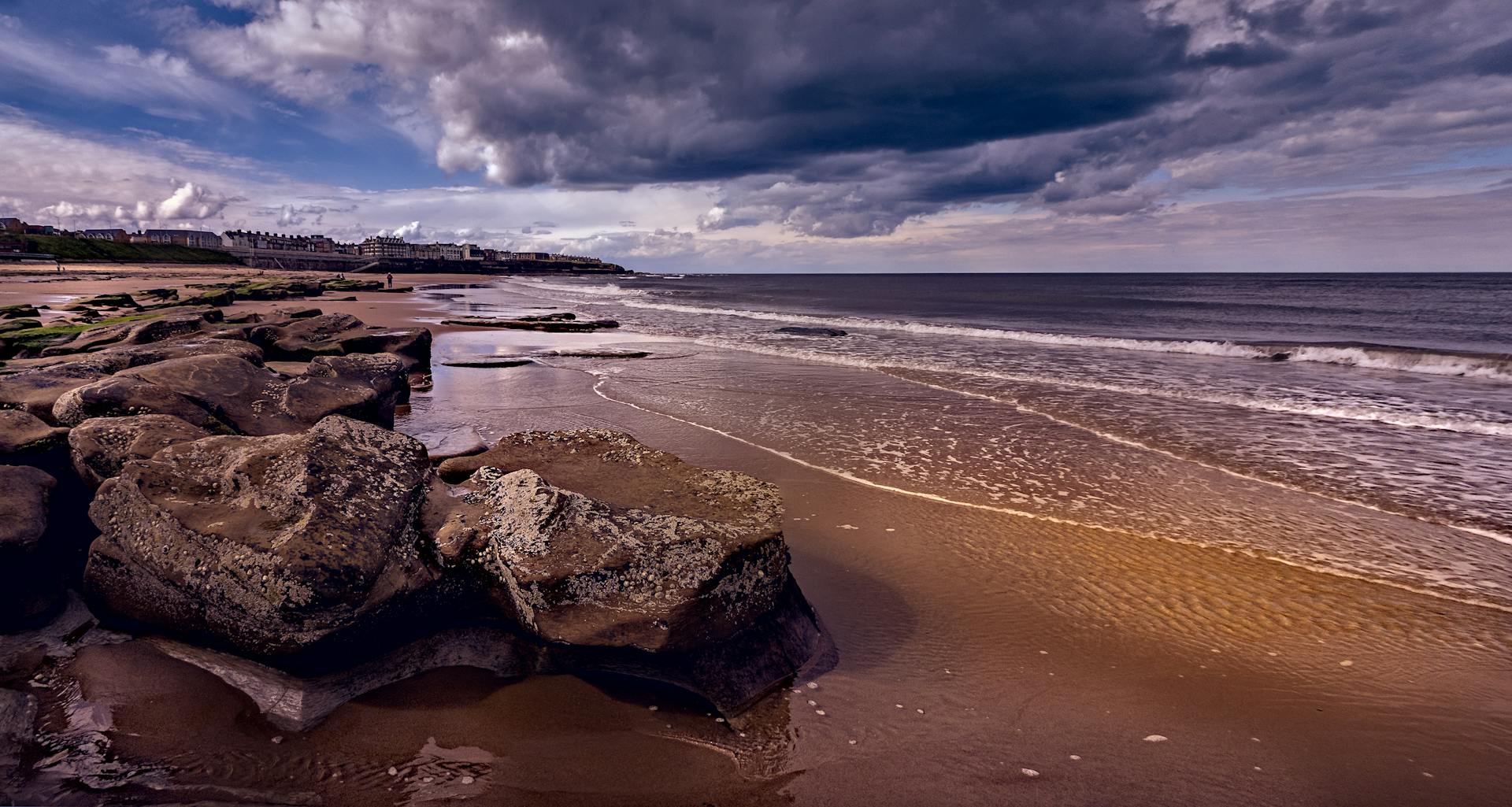 Serene beach scene with dramatic clouds and rock formations on the coast.