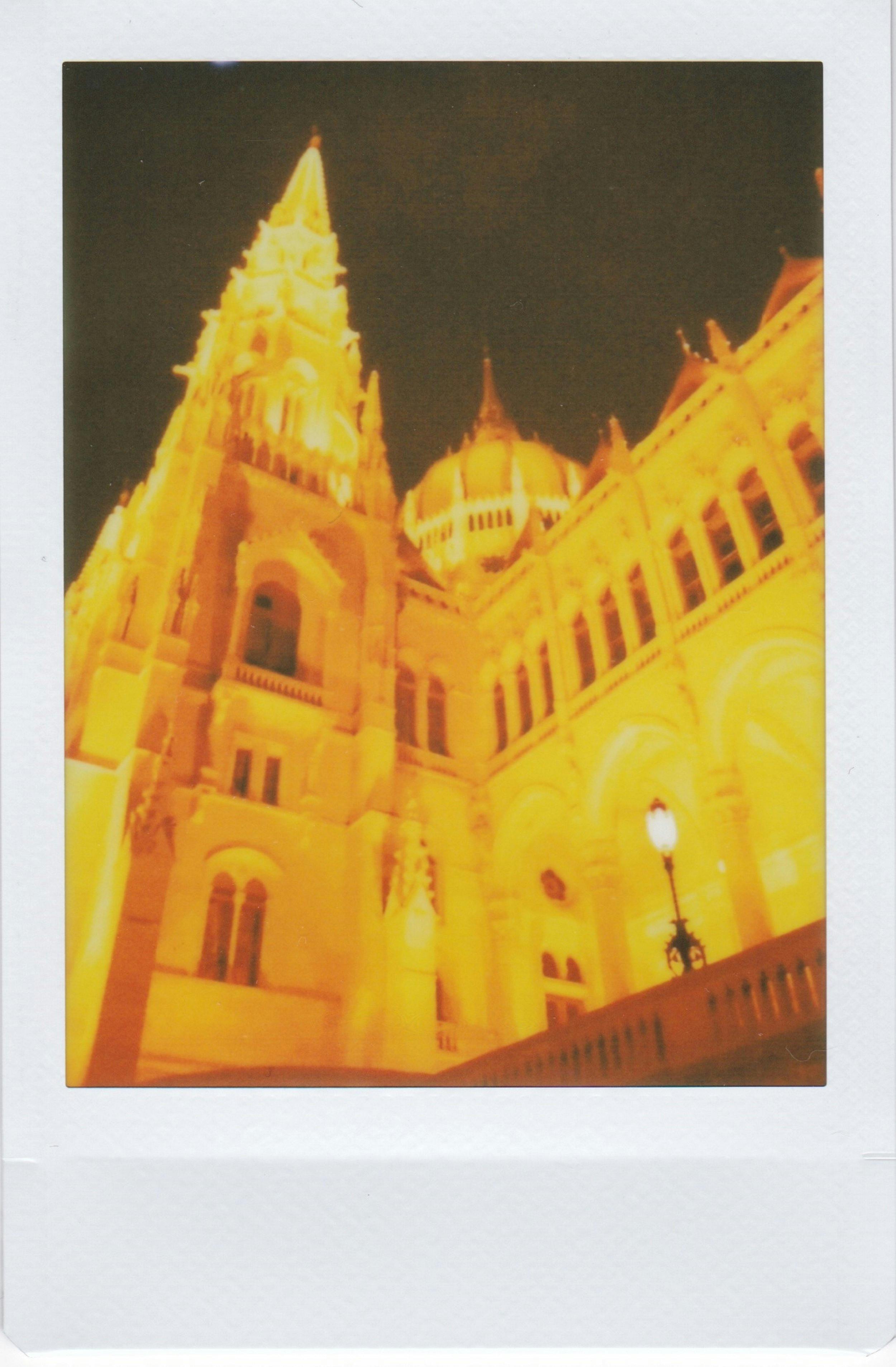 Instant photo capturing the illuminated Hungarian Parliament Building at night.