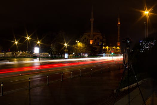 Long exposure of city traffic creating vibrant light trails against a mosque backdrop at night.
