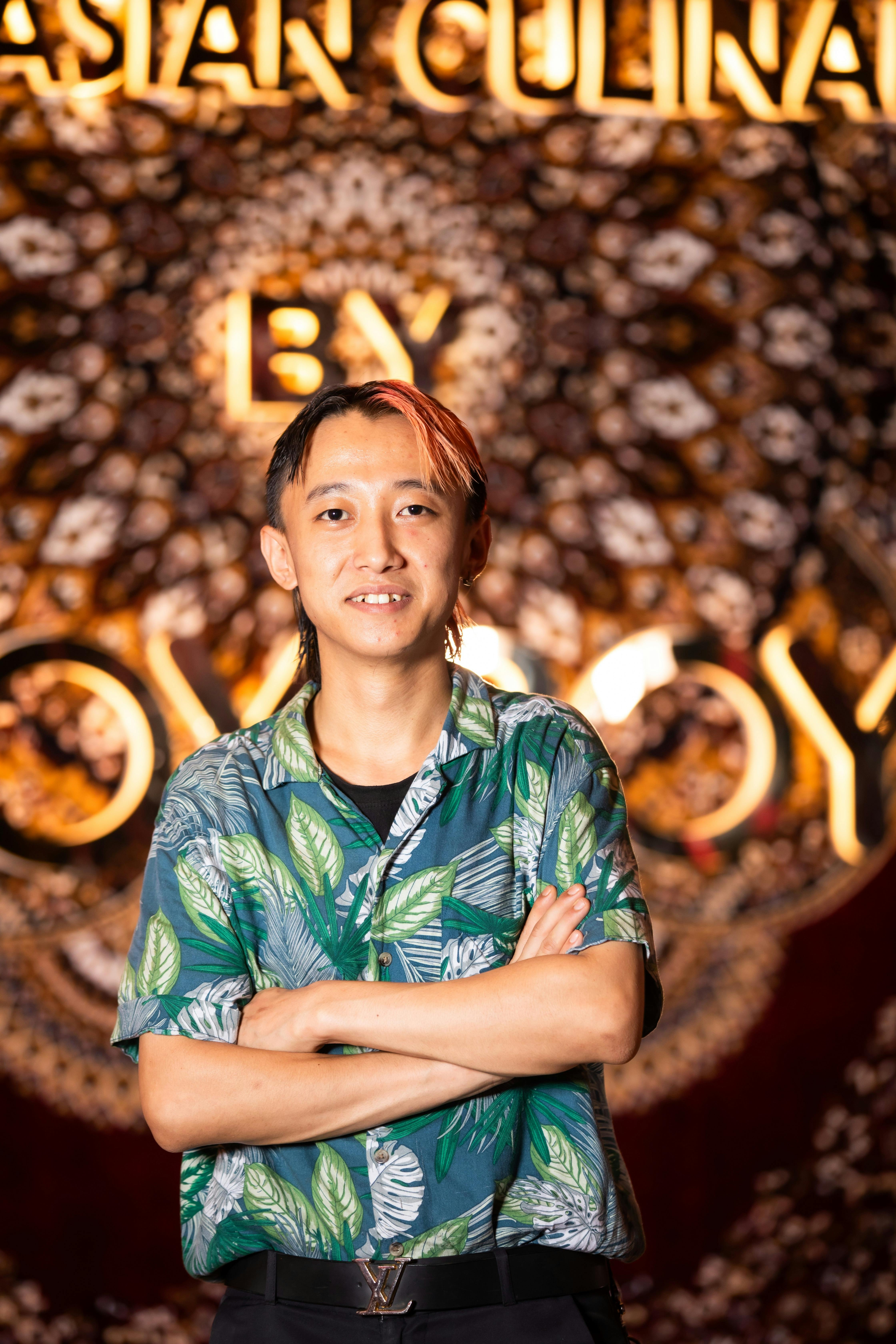 Smiling man in tropical shirt stands confidently with vibrant indoor background.