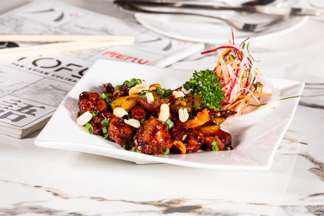 Tasty Kung Pao chicken dish served on a white plate with garnish, showcasing vibrant colors and textures.
