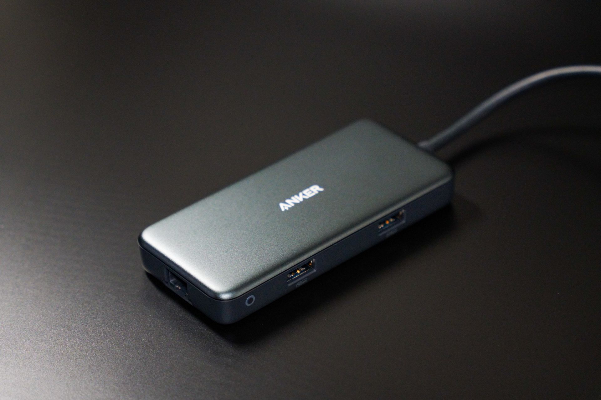 Compact USB-C hub on dark desk surface with visible USB ports.