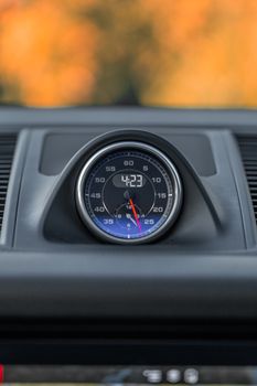 Focus on a car dashboard clock with blurred autumn background.