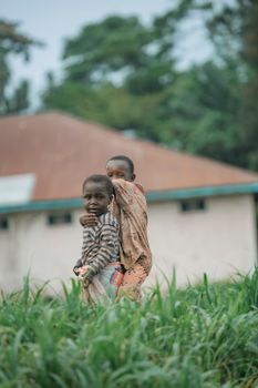 Two children playing outdoors in a village setting, surrounded by lush greenery.