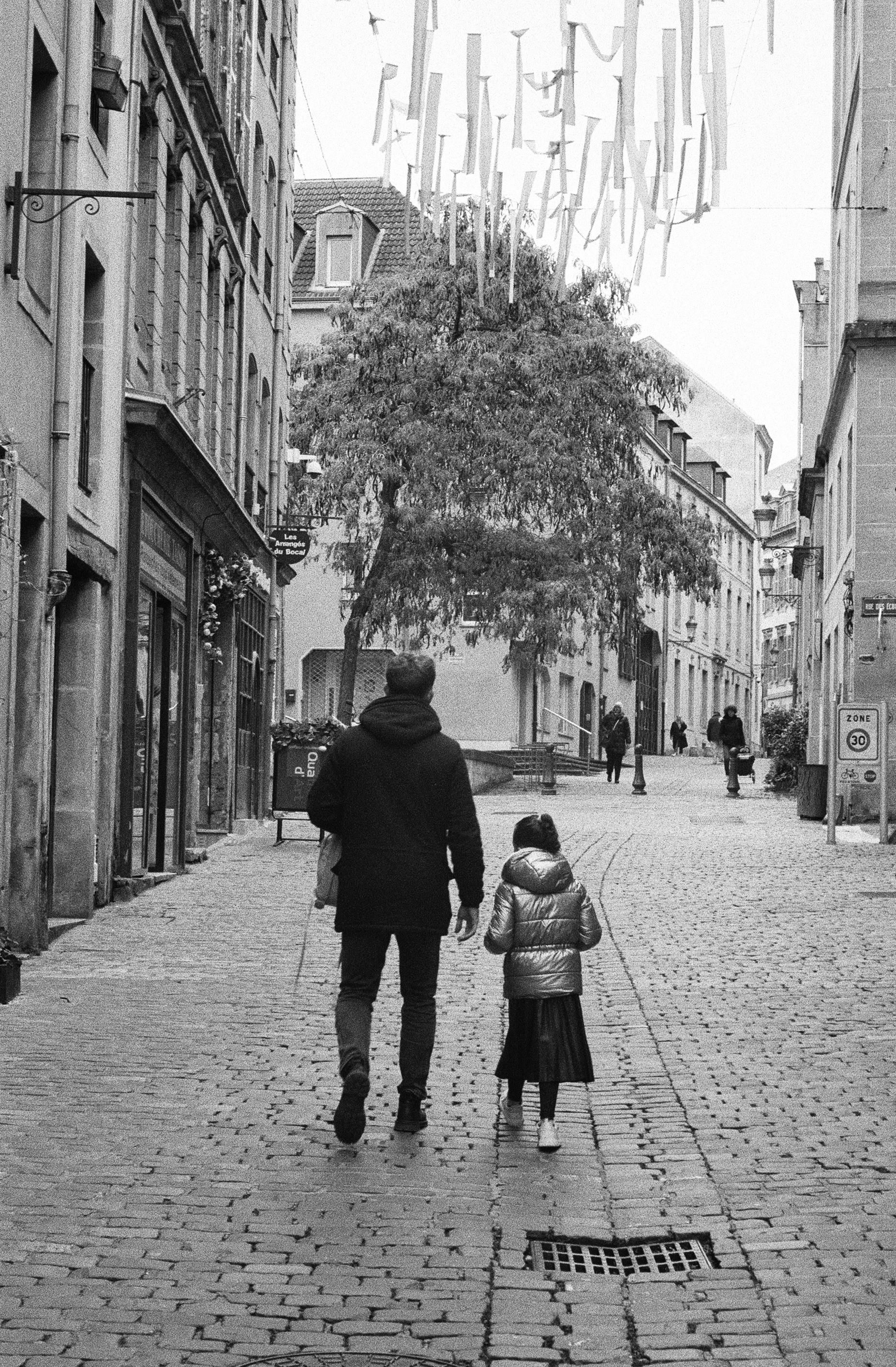 Black and white scene of a father and daughter walking in Metz, France.