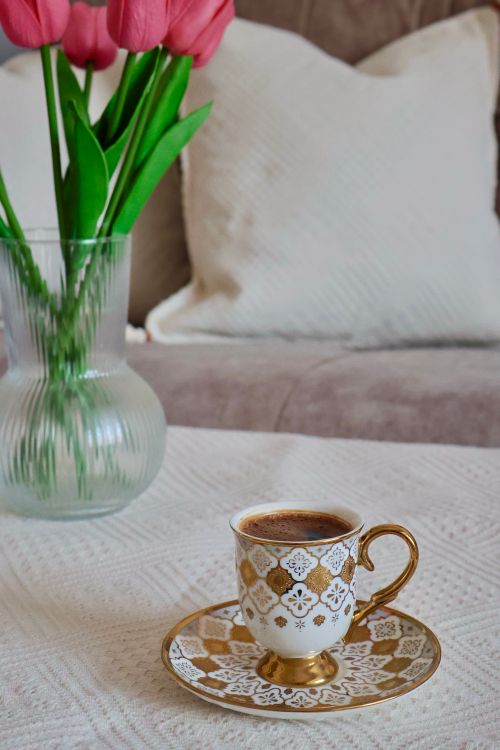 Free A stylish coffee cup with gold trim sits near vibrant tulips in a cozy living room. Stock Photo