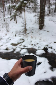 A person holding a hot beverage cup in a snowy forest, evoking warmth and tranquility.