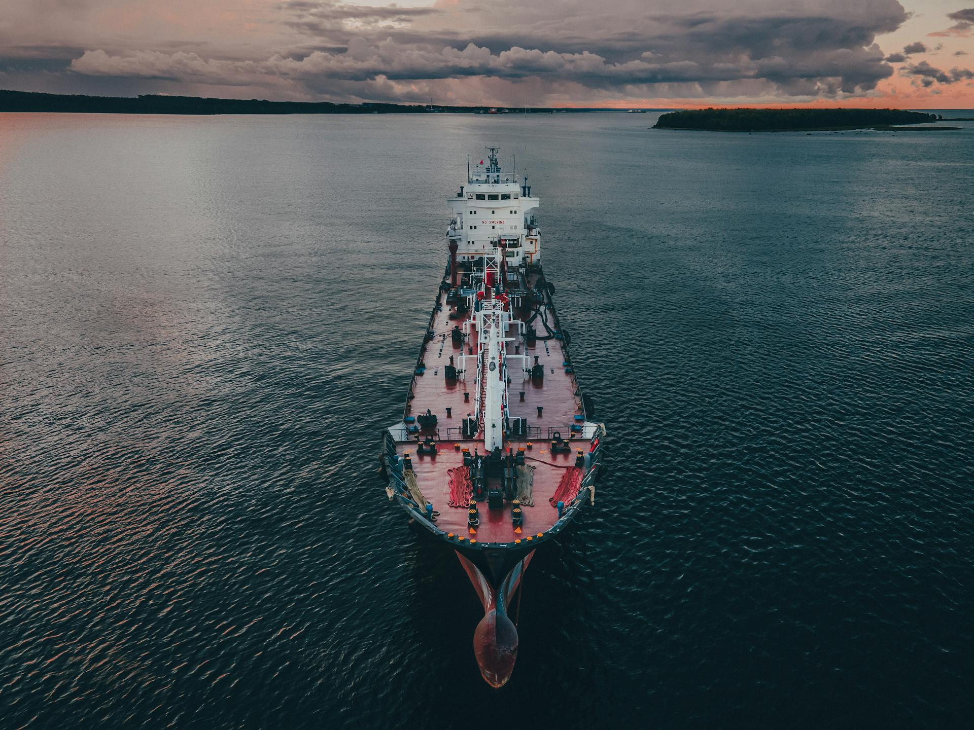 Aerial shot of a cargo ship navigating the calm ocean waters under twilight skies.