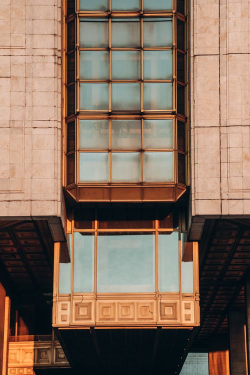 Free Close-up of a modern building facade with prominent glass window design, capturing warm sunlight. Stock Photo