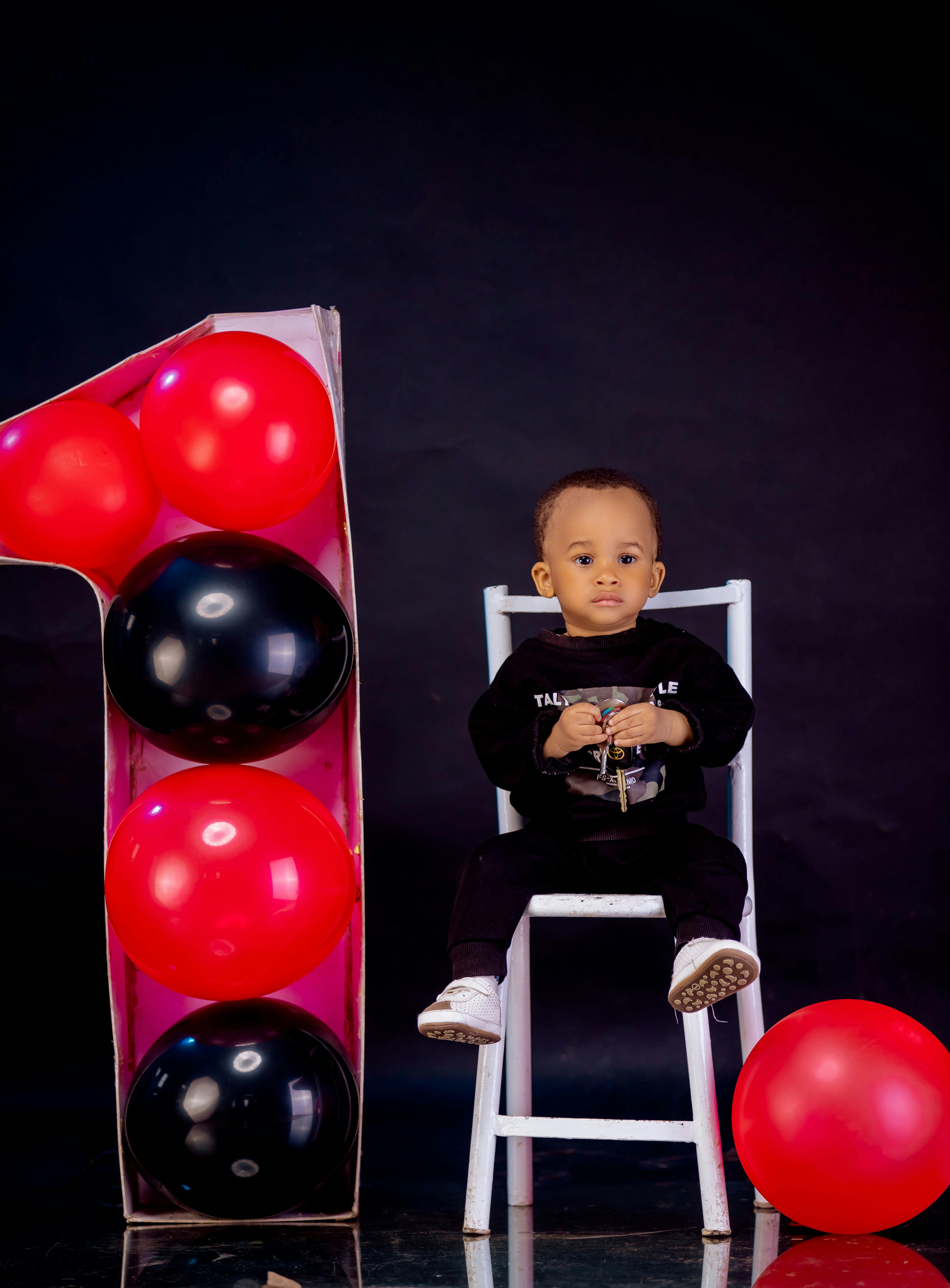 Adorable baby sitting with red and black balloons for a first birthday.