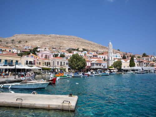 Free Scenic view of a picturesque Greek harbor town with colorful boats and hillside houses under a blue sky. Stock Photo