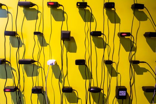 Power adapters casting shadows on a vibrant yellow wall, creating a geometric pattern.