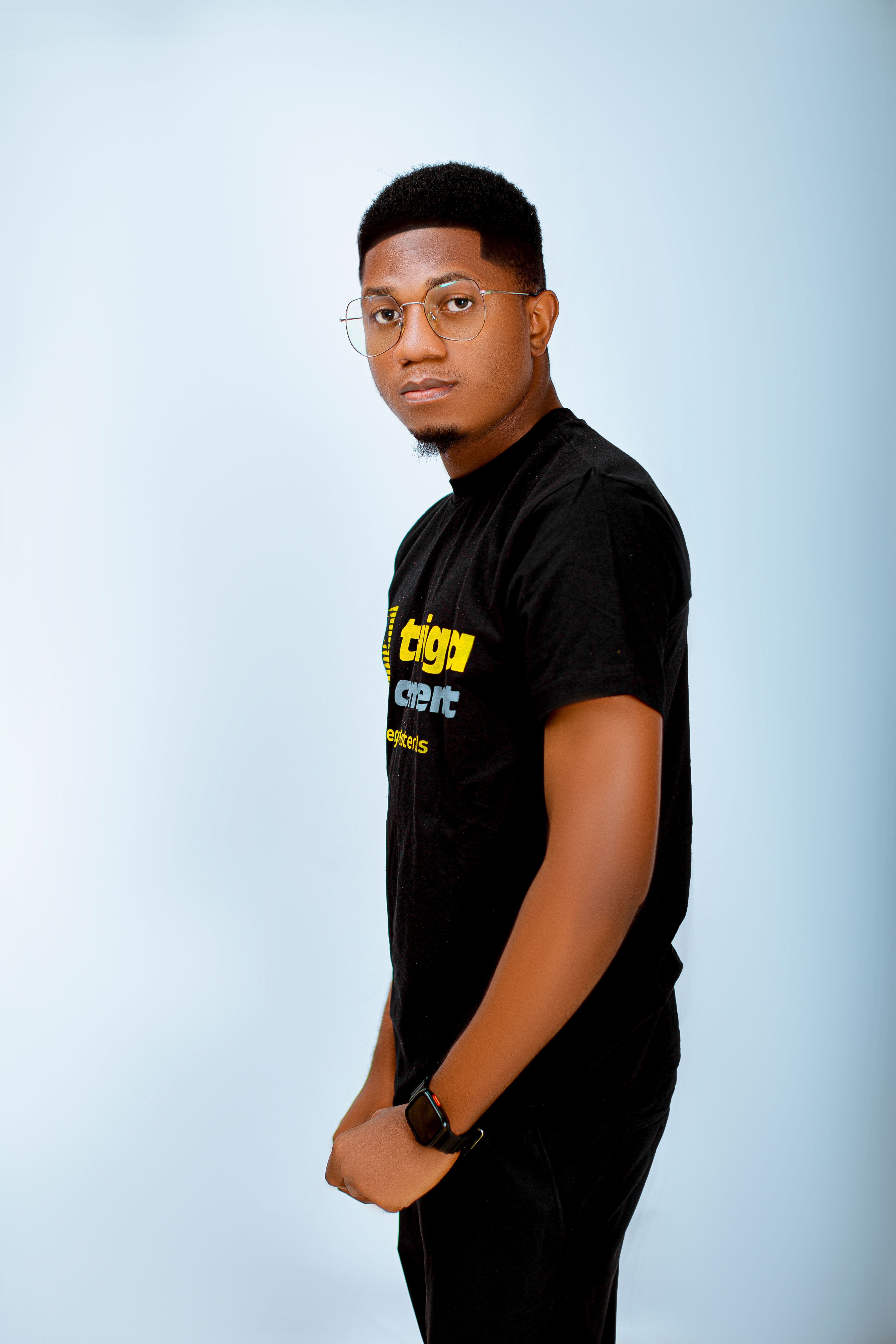 Studio portrait of young man wearing glasses and a black T-shirt, standing against a light background.