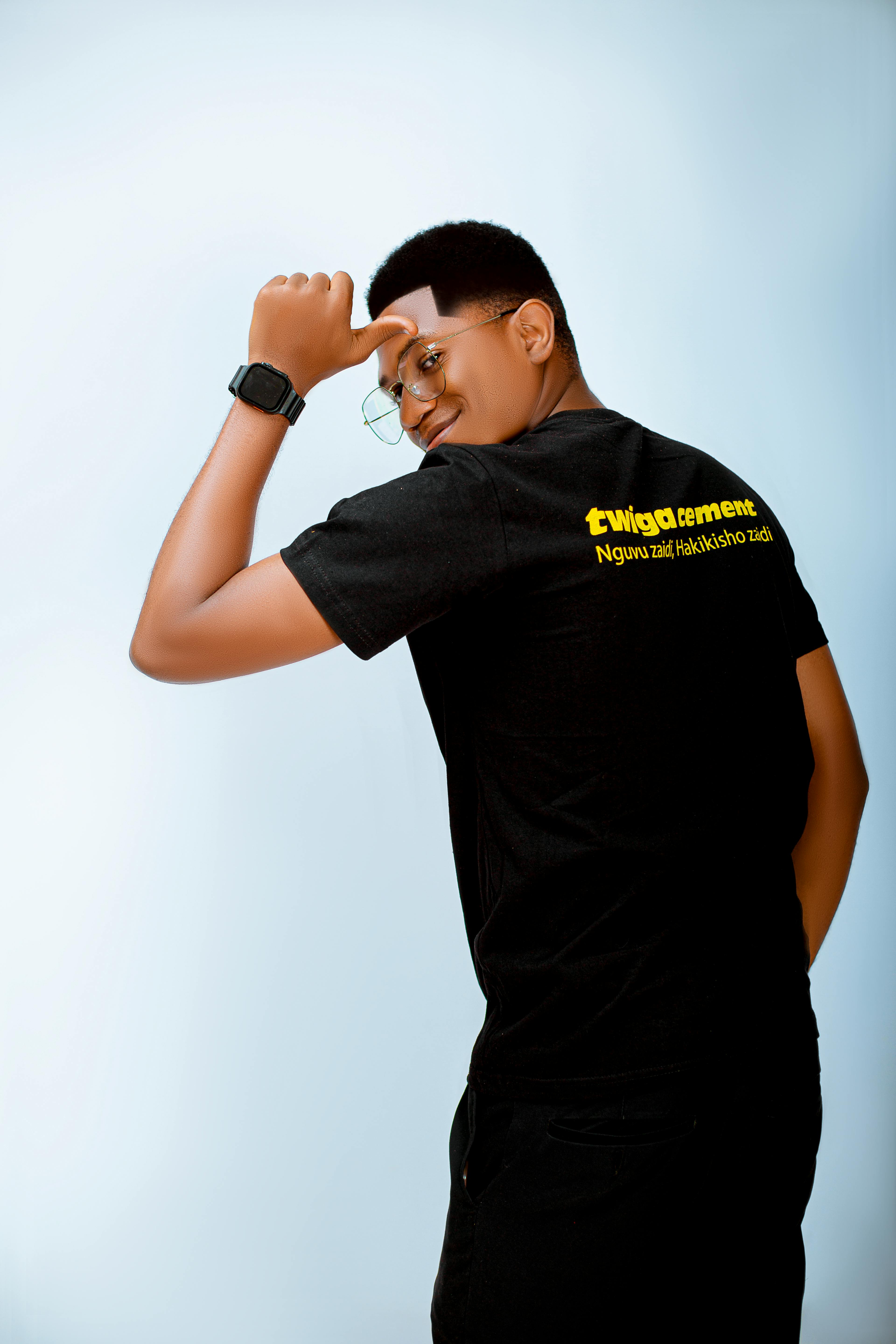 Young adult in black t-shirt with text posing confidently against light background.