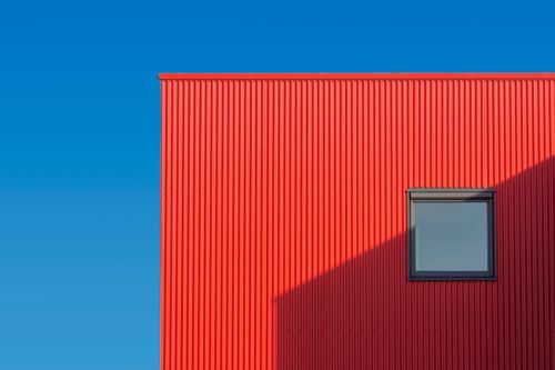 Free Minimalist red building facade with a window and strong shadows under a clear blue sky. Stock Photo
