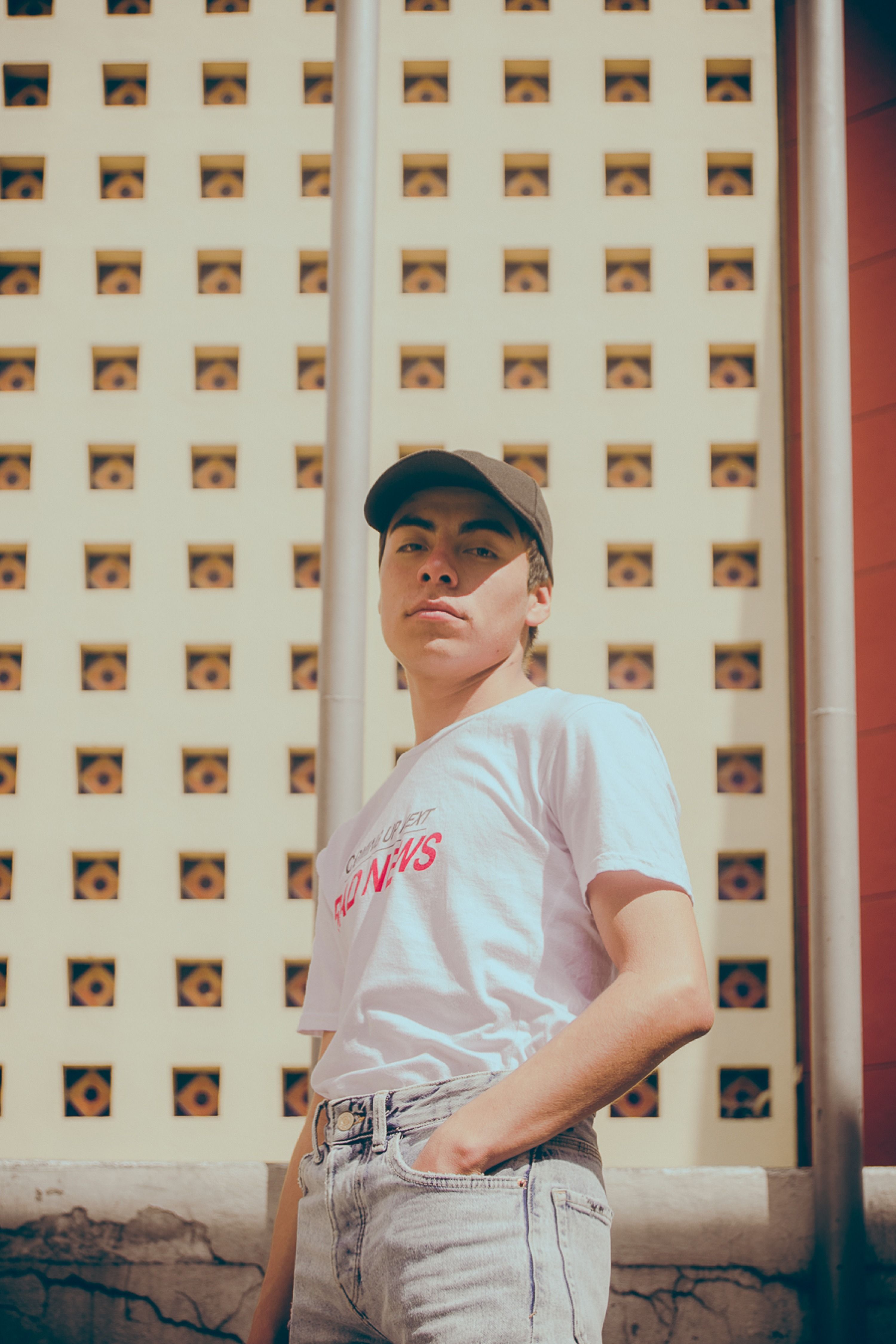 A stylish young adult poses confidently in casual urban streetwear against a modern architectural backdrop.