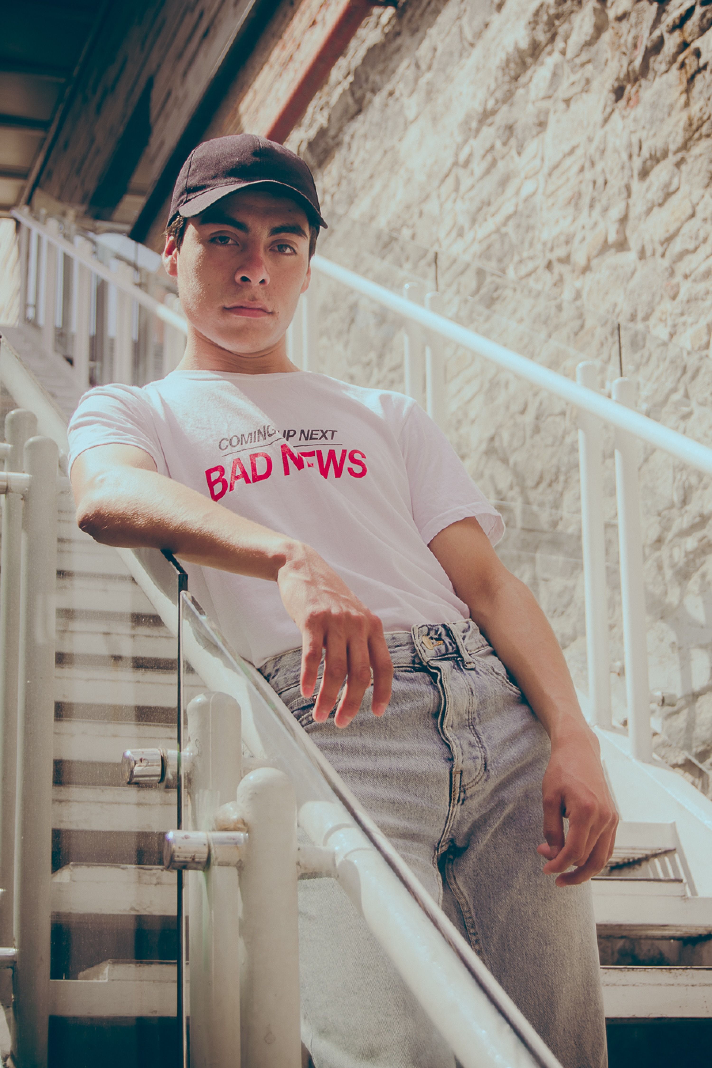 Young man in casual attire poses on urban outdoor stairs, projecting confidence.