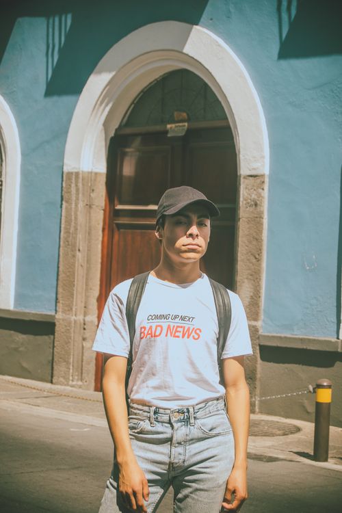 Free Man in casual clothing stands outside a blue building in sunny setting. Stock Photo