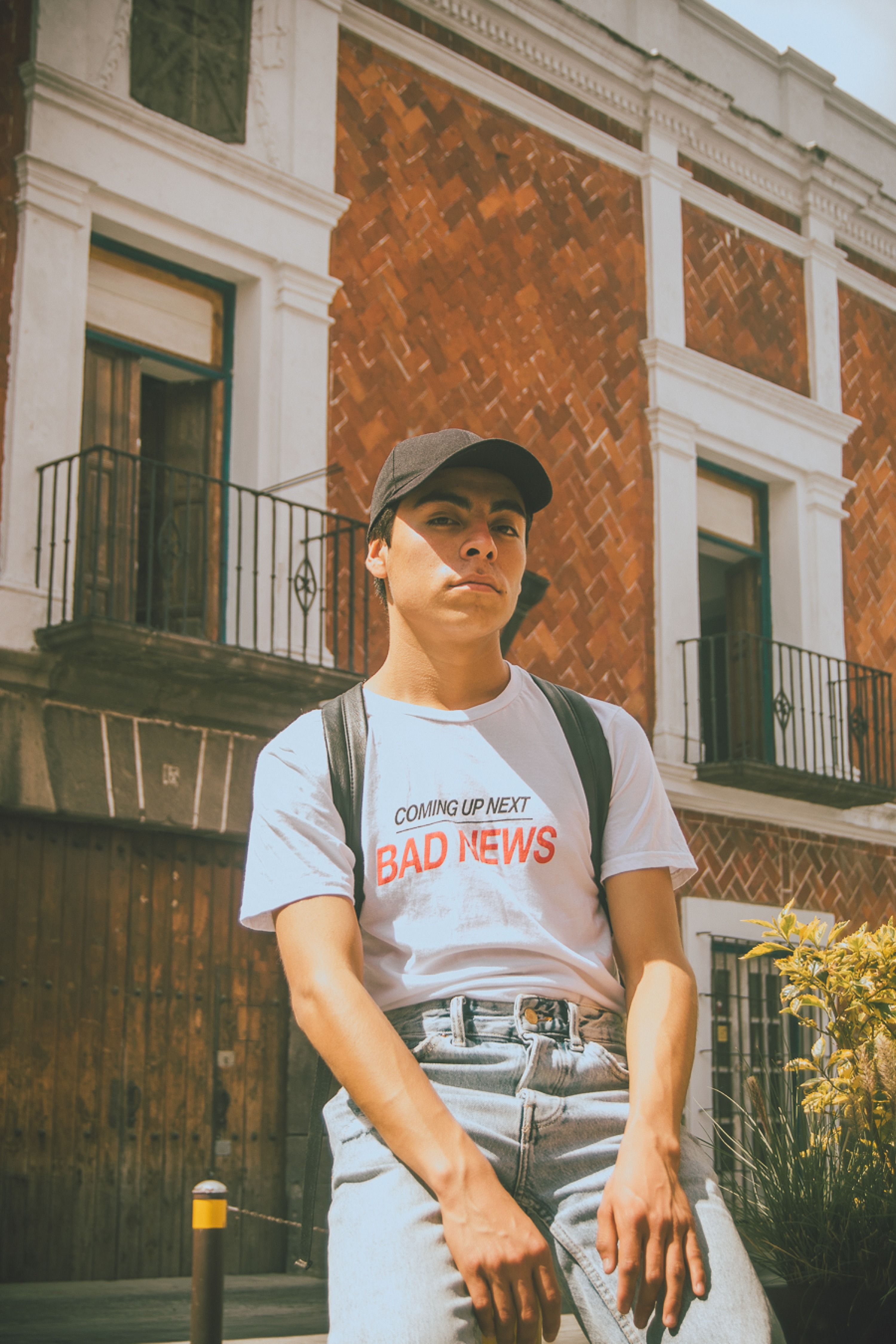 A young adult poses in an urban street wearing a t-shirt with 'Bad News' text.