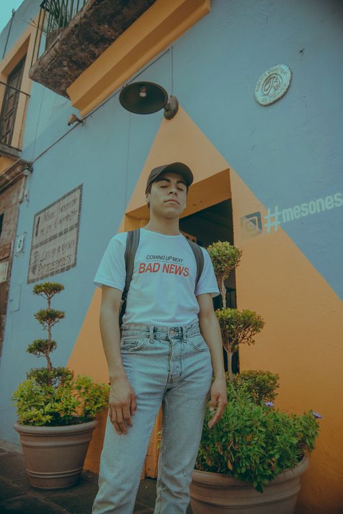 Free Young adult in stylish outfit poses against colorful urban backdrop, with bold graphic tee. Stock Photo