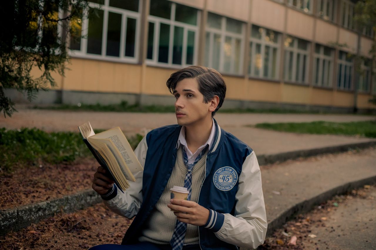 a young man reading a book and holding a coffee cup on a college campu