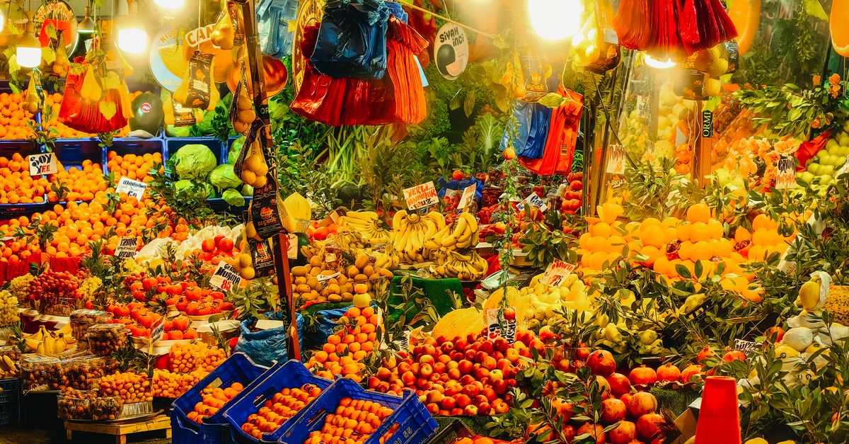 Student walking through a bustling Amman market with fresh fruits and vegetables