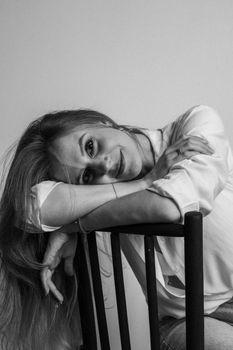 Elegant black and white portrait of a woman leaning on a chair indoors.