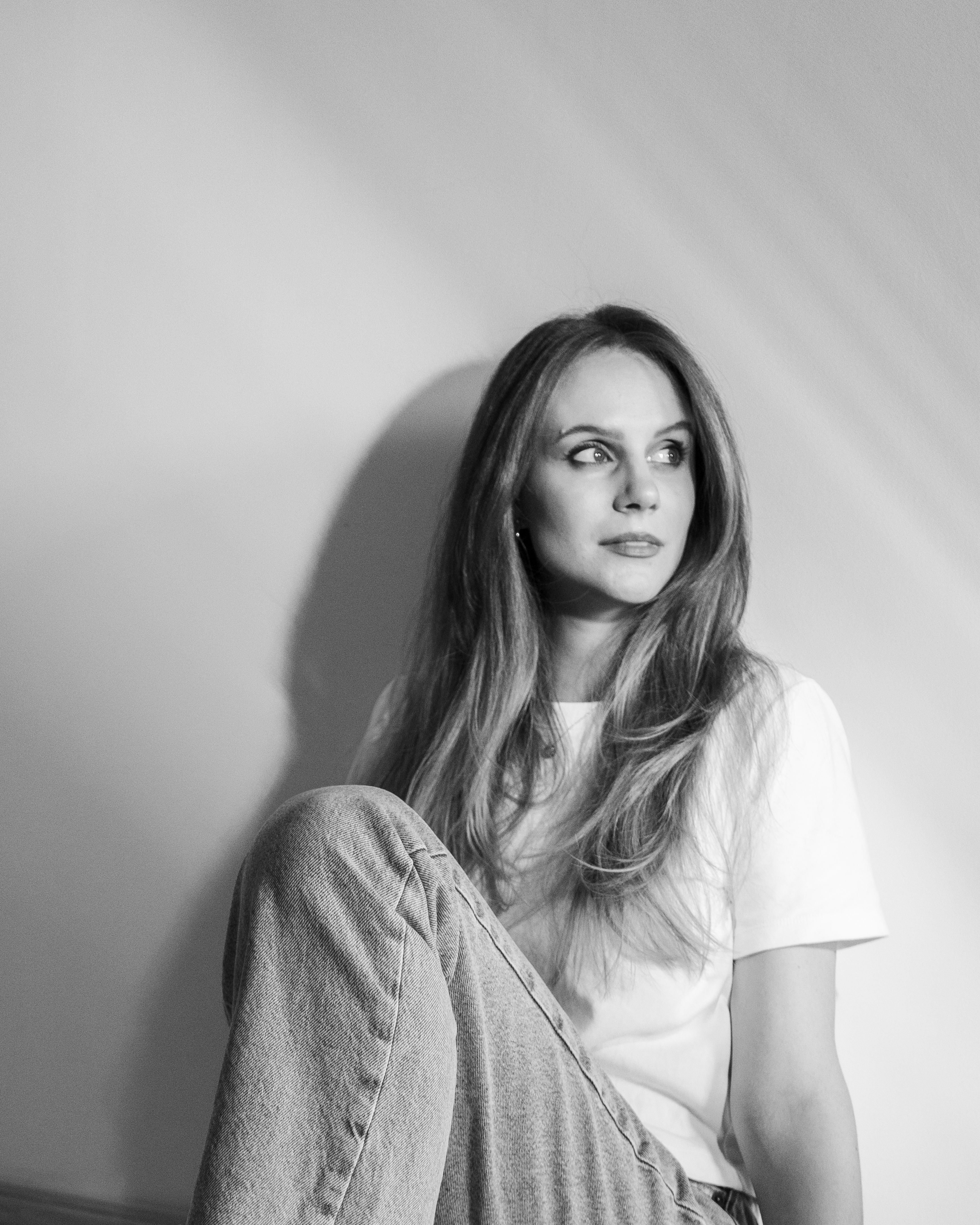 Elegant black and white portrait of a young woman sitting against a wall.