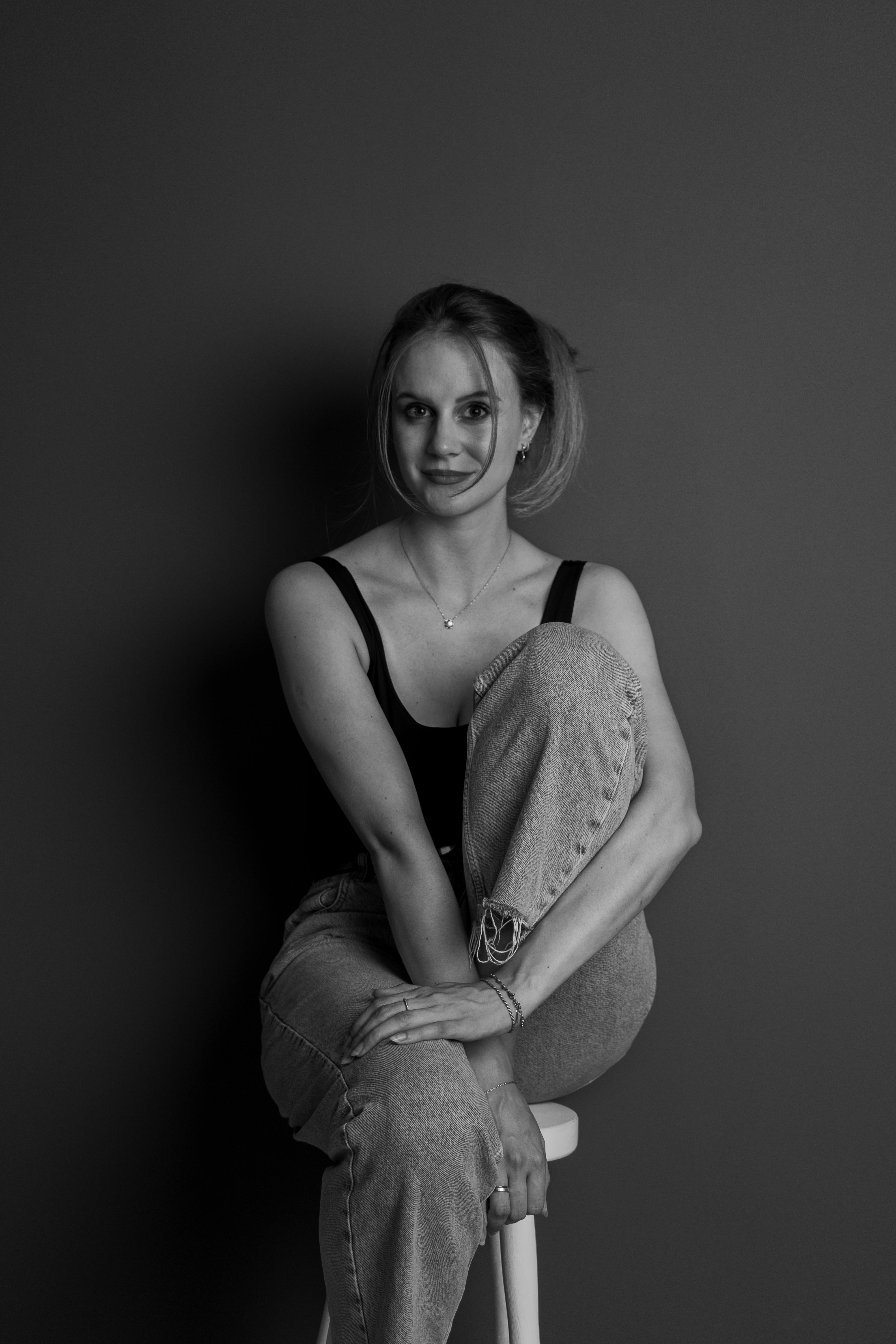 Elegant black and white portrait of a woman seated on a stool.