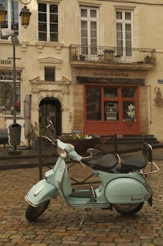 A classic blue scooter parked on cobblestones in front of historical European buildings.