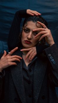 Dark and moody portrait of a woman in stylish attire with dramatic hand pose.