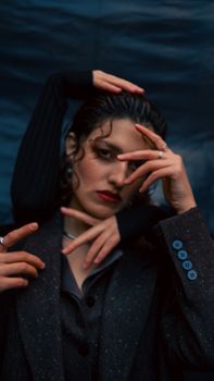 A woman in a suit with dramatic hand gestures against a dark background.
