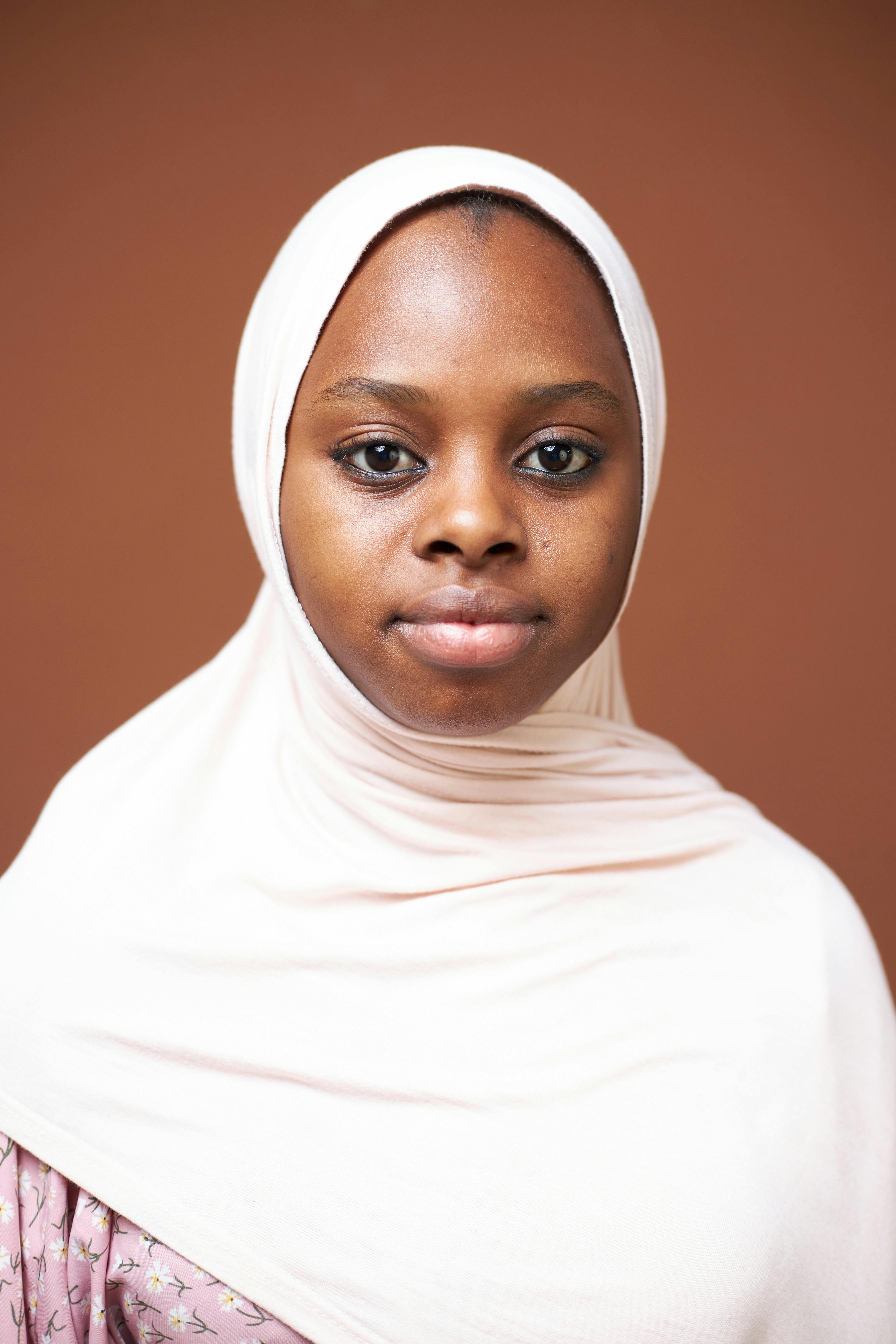 Portrait of a young woman wearing a hijab, standing against a plain background.