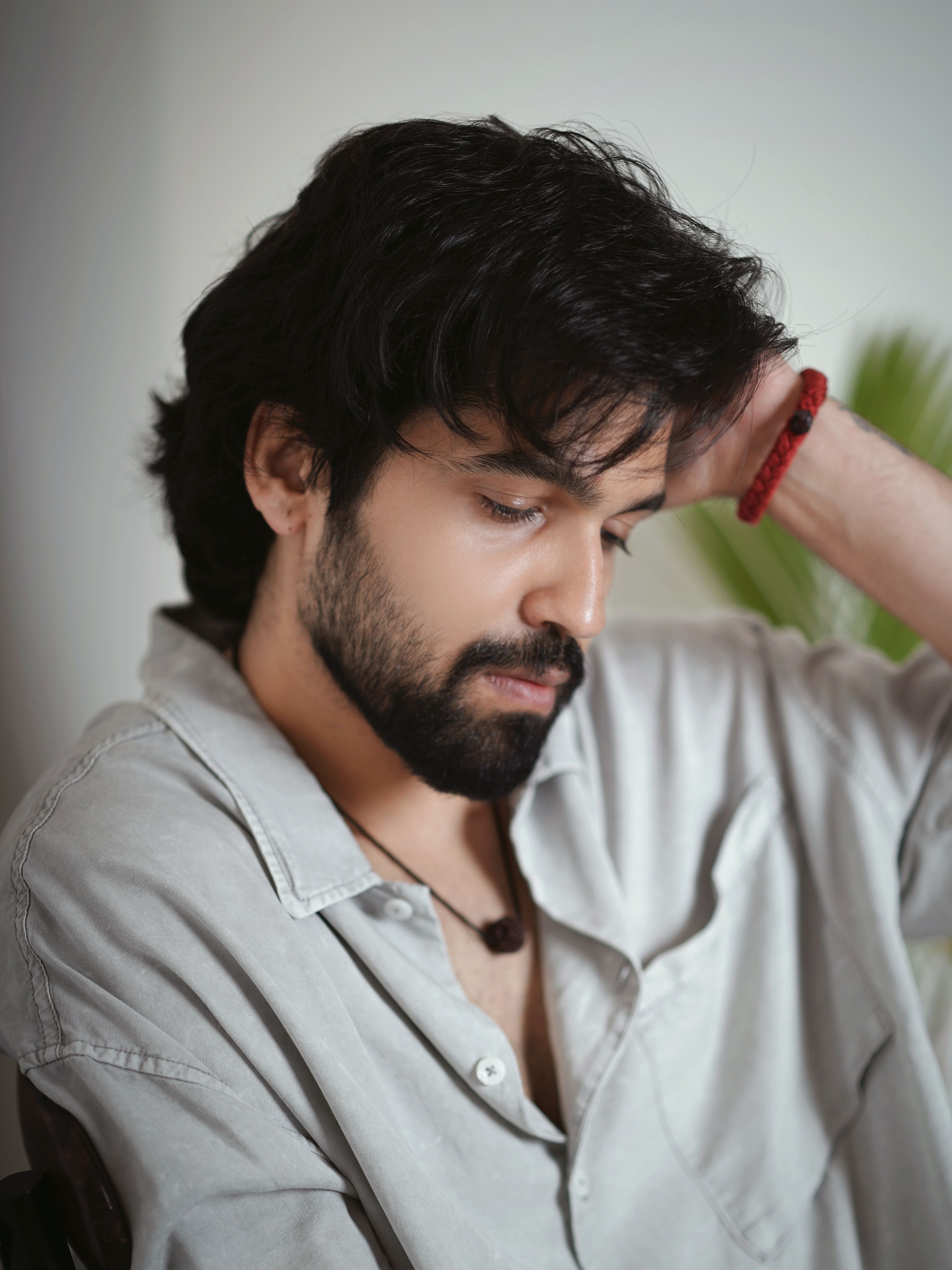 Pensive young man in a relaxed pose, wearing a casual shirt, indoors.