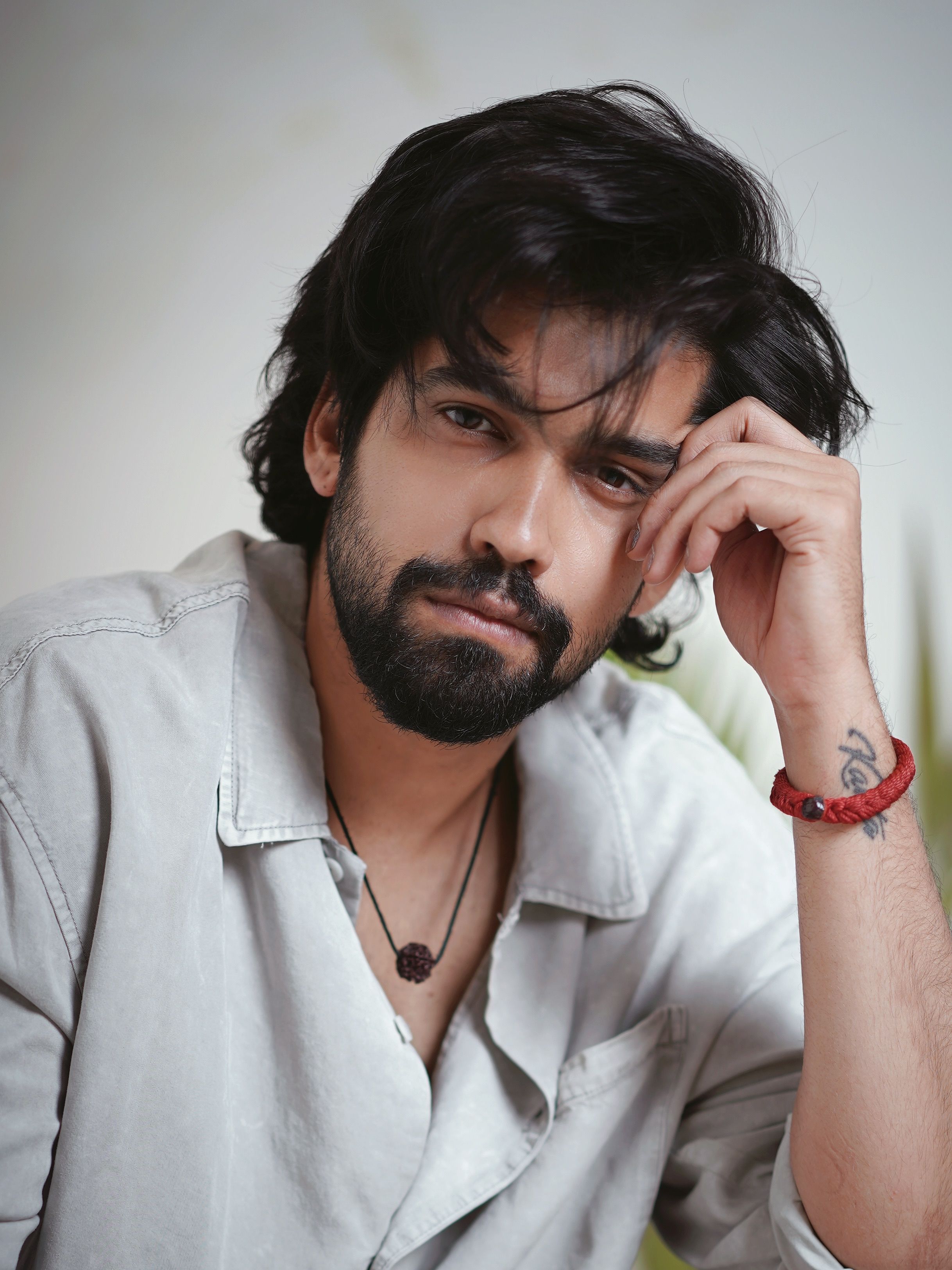 Portrait of a thoughtful man in casual attire, showcasing a tattoo and fashionable hairstyle.