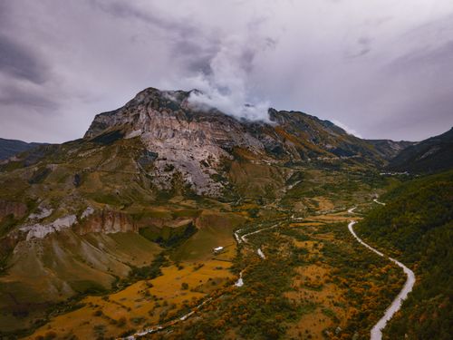 Free Aerial shot of a scenic mountain landscape with a winding river and cloudy sky. Stock Photo