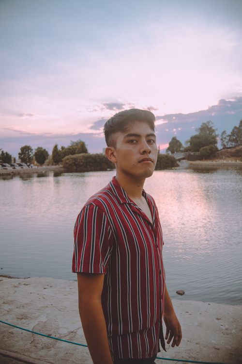 Free Portrait of a young man by a tranquil lake during sunset, capturing a calm and reflective moment. Stock Photo