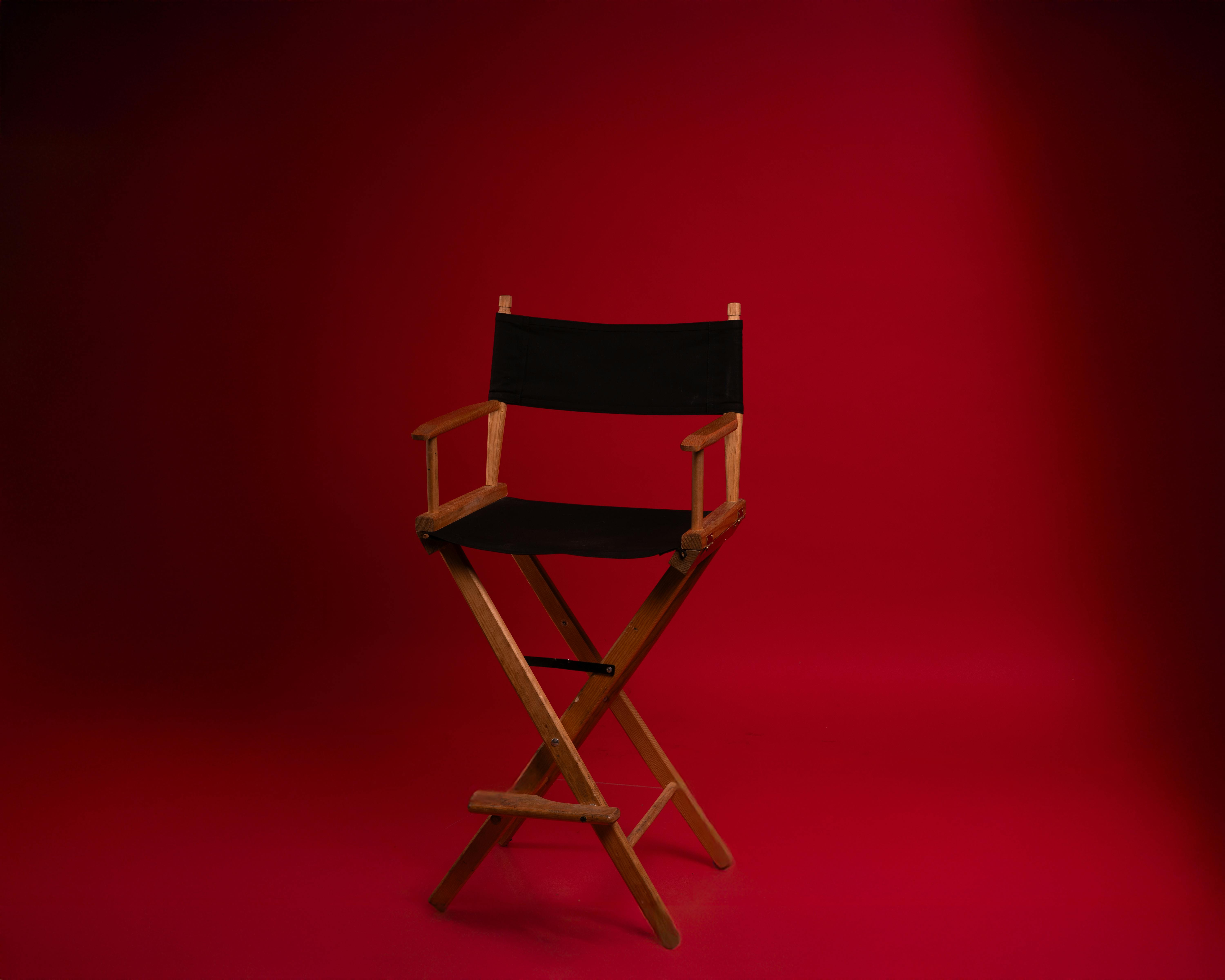 De franc Una cadira de director de fusta sobre un fons vermell vibrant, que simbolitza l'autoritat de la indústria cinematogràfica. Foto d'estoc