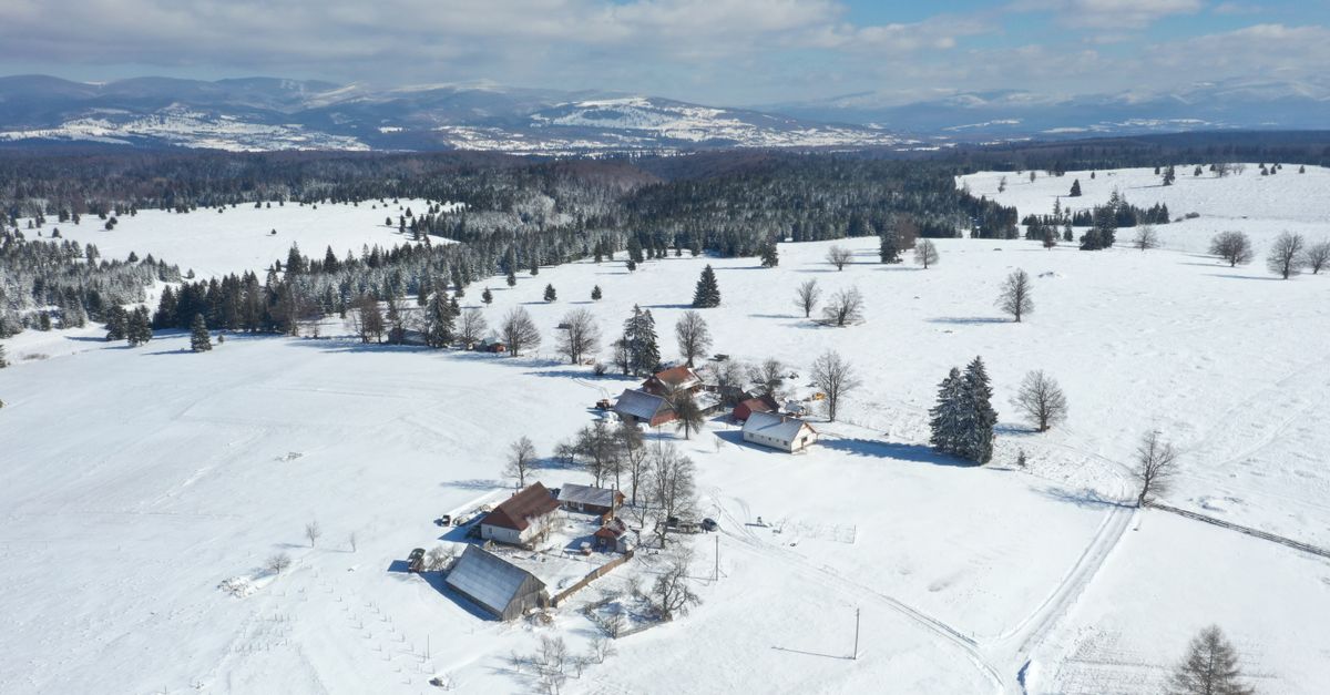 Aerial shot of a snow-covered village in Harghita County, Romania, with distant mountains.