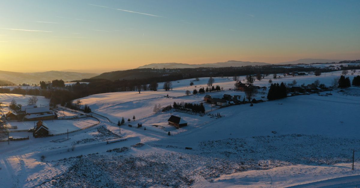 Captivating aerial view of Fântâna Brazilor, Harghita, Romania, with snow-covered fields at sunset.