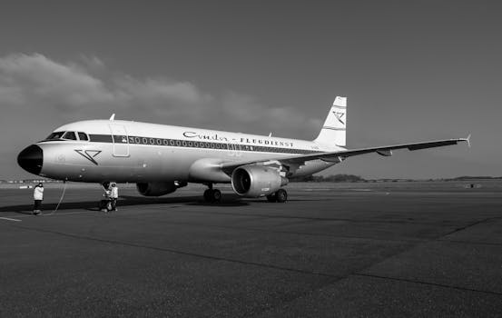 Monochrome image of a parked airplane on an airport runway with passengers boarding.
