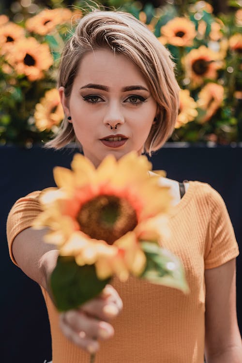 Selective Focus Photo of Woman in Orange Top Holding Out Sunflower