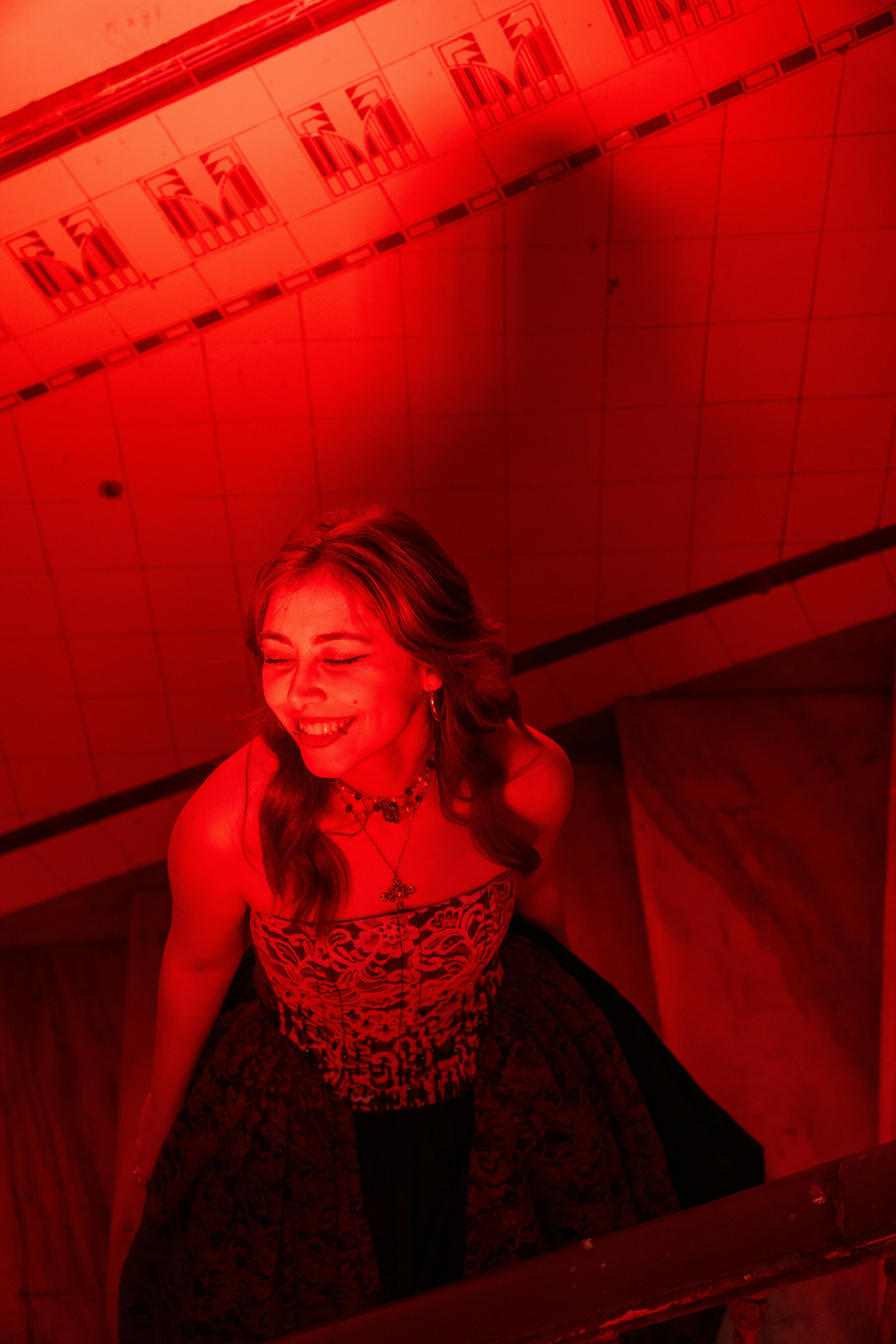 Bezpłatne Kobieta w sukience bez ramiączek cieszy się chwilą na schodach skąpanych w czerwonym świetle. Zdjęcie z galerii