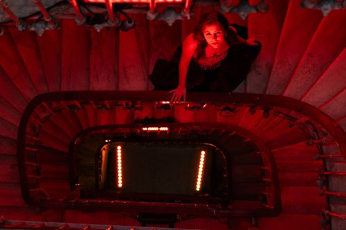 Free A woman in a dress captured dramatically on a spiral staircase with red lighting. Stock Photo