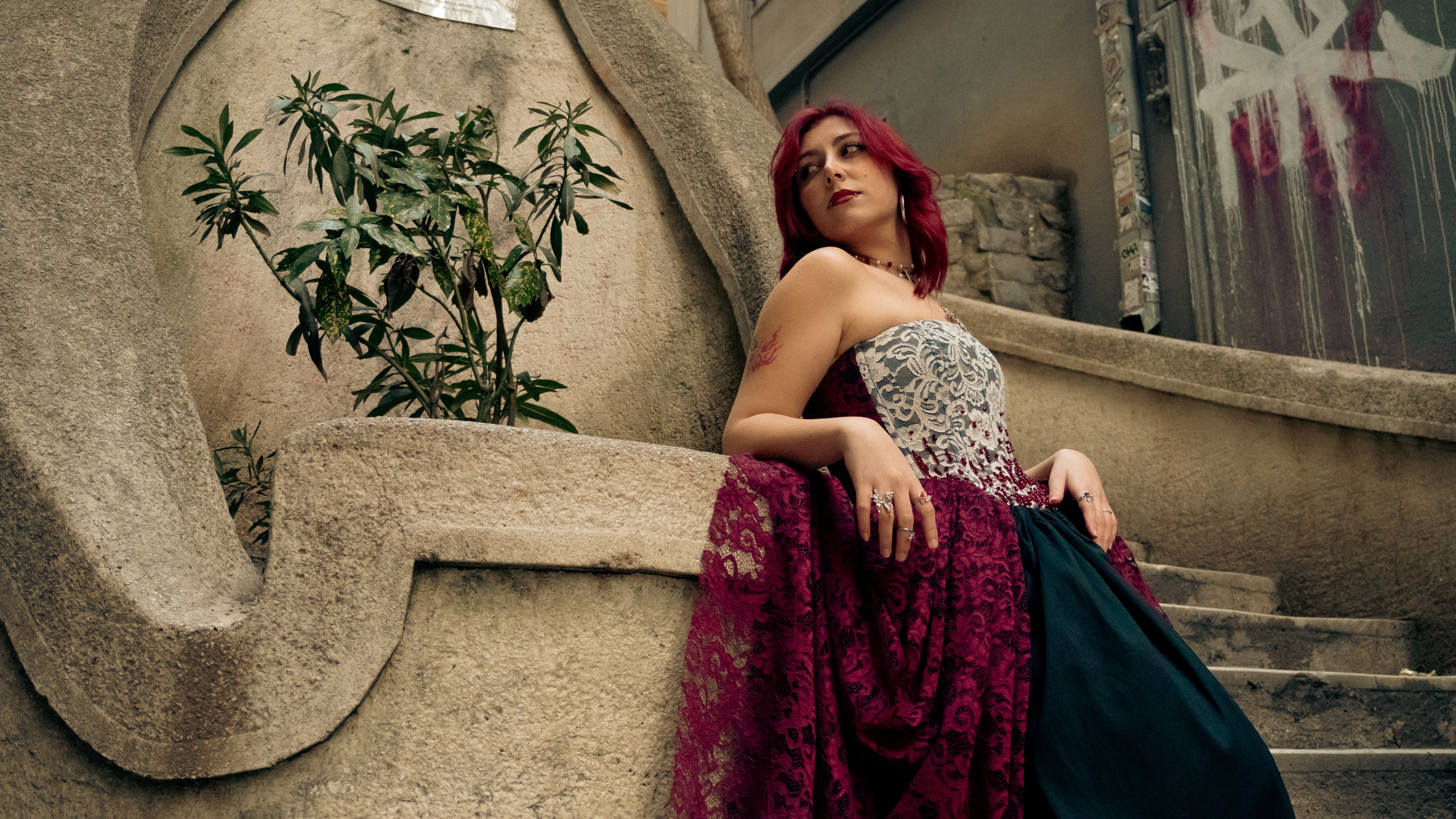 A woman in a luxurious gown poses on stone steps, exuding elegance and style.