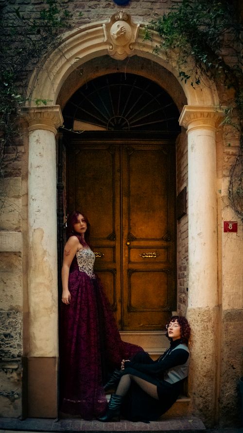 Free Two women in vintage dresses stand by a vintage wooden doorway, exuding elegance. Stock Photo